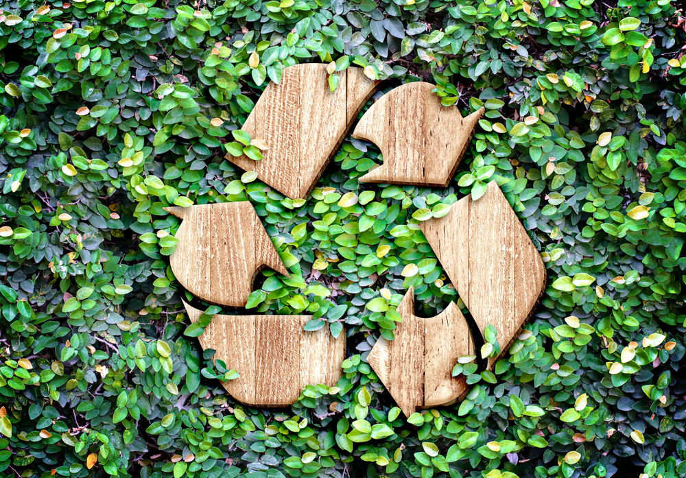 A wooden recycling symbol surrounded by leaves.